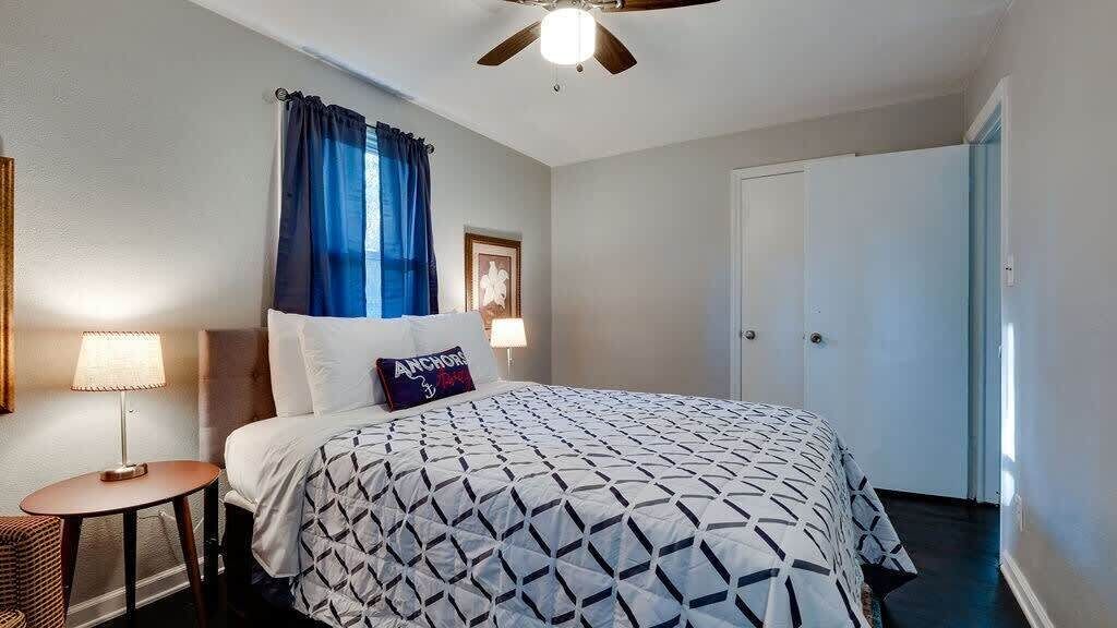 A bedroom with a bed, a nightstand, a lamp, a ceiling fan, and a door.