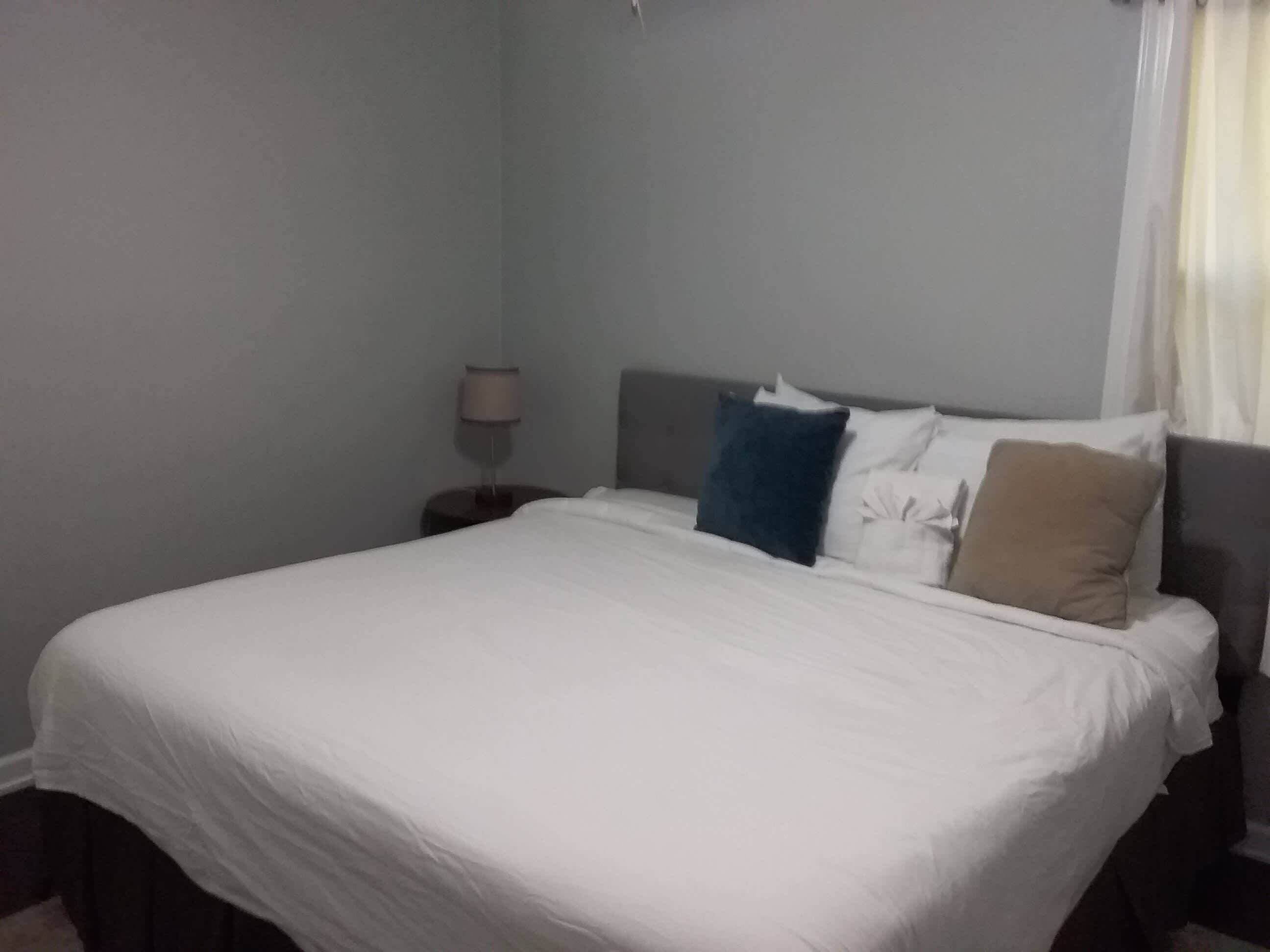A neatly made bed with white bedding, a dark headboard, and a bedside lamp.