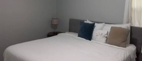A neatly made bed with white bedding, a dark headboard, and a bedside lamp.