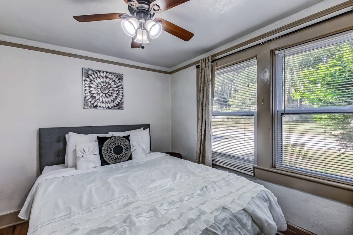 A bedroom with a bed, a ceiling fan, a wall decoration, and windows with blinds.