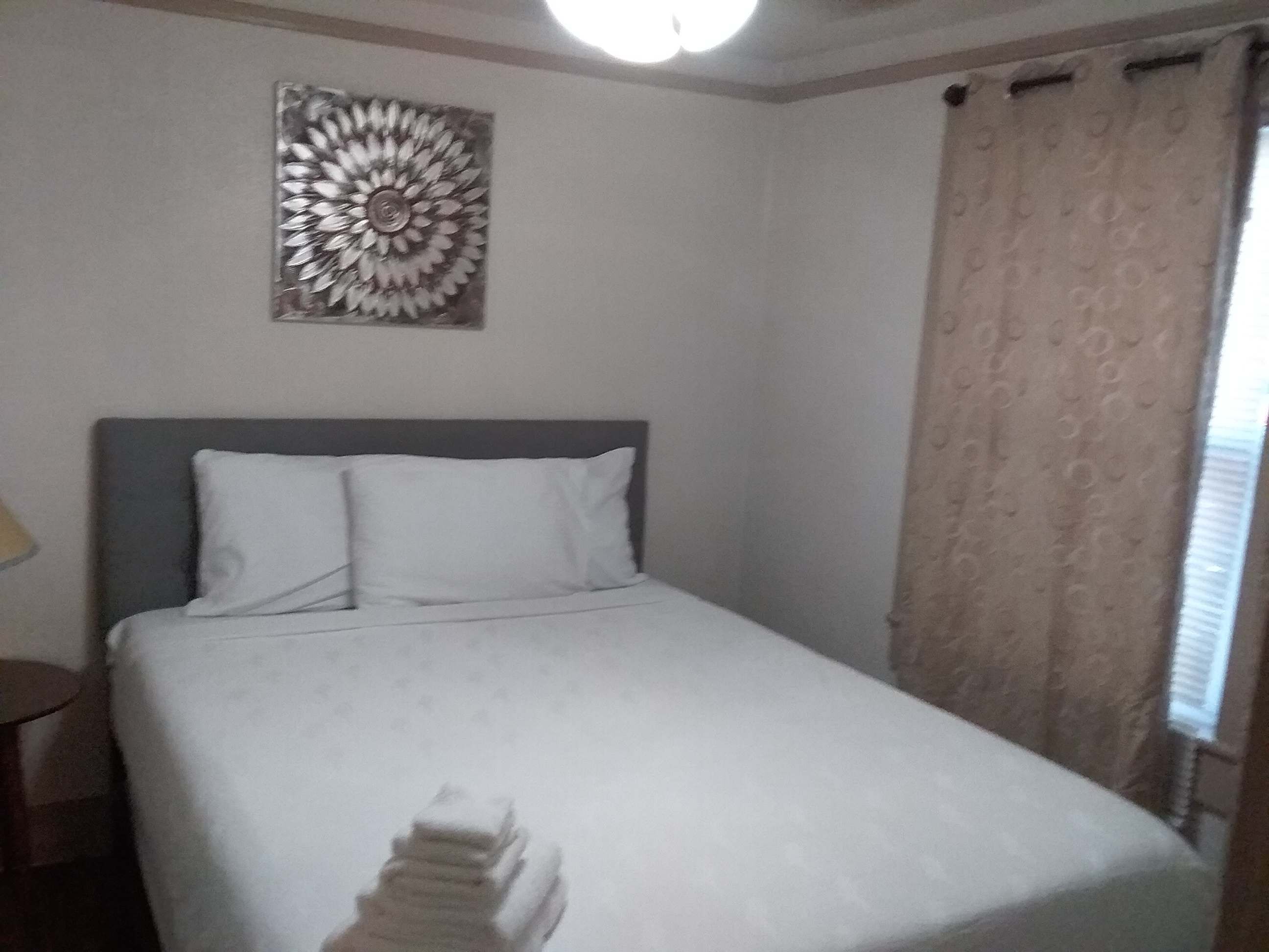A neatly made bed with white bedding, a gray headboard, and a decorative wall piece above it.