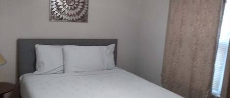 A neatly made bed with white bedding, a gray headboard, and a decorative wall piece above it.