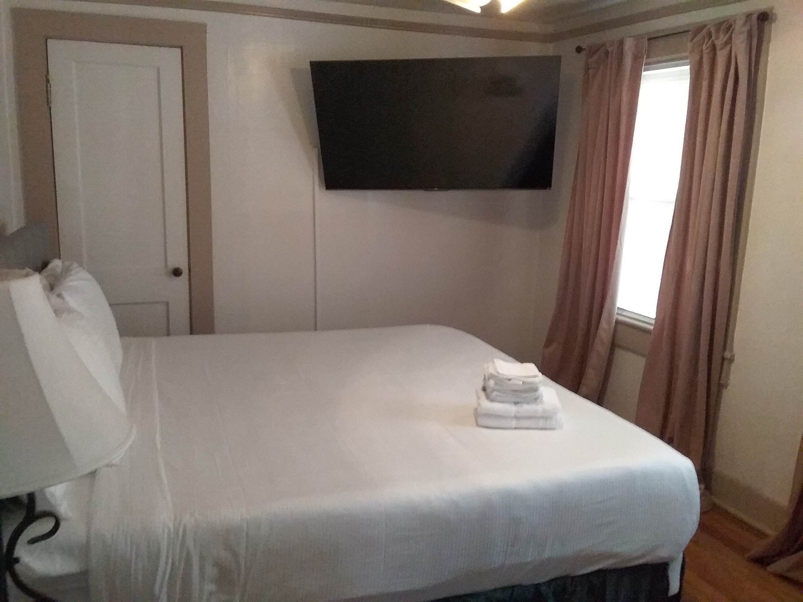 Une chambre d’hôtel avec un lit, un téléviseur fixé au mur, une porte et une fenêtre avec des rideaux.