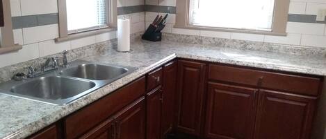 A kitchen with two sinks, wooden cabinets, a marble countertop, and a window with blinds.