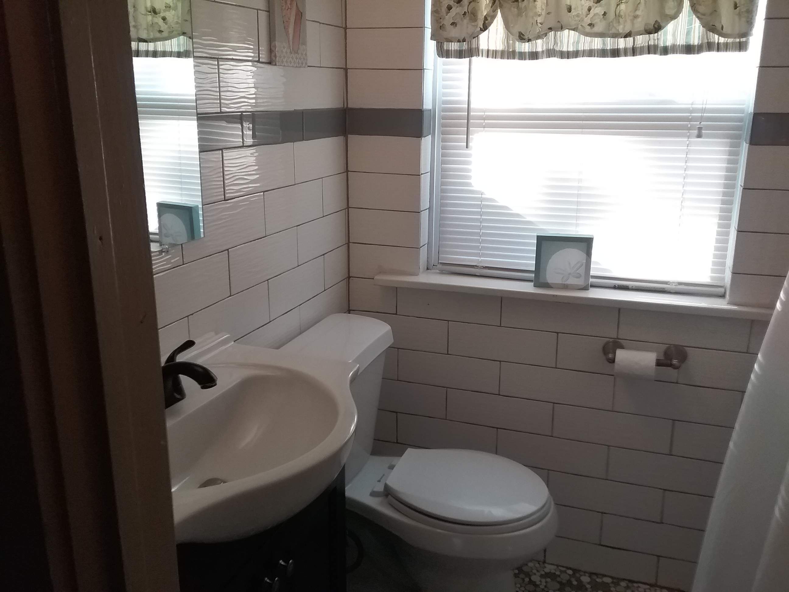 Et lille badeværelse med en hvid vask, toilet og et vindue med persienner.
