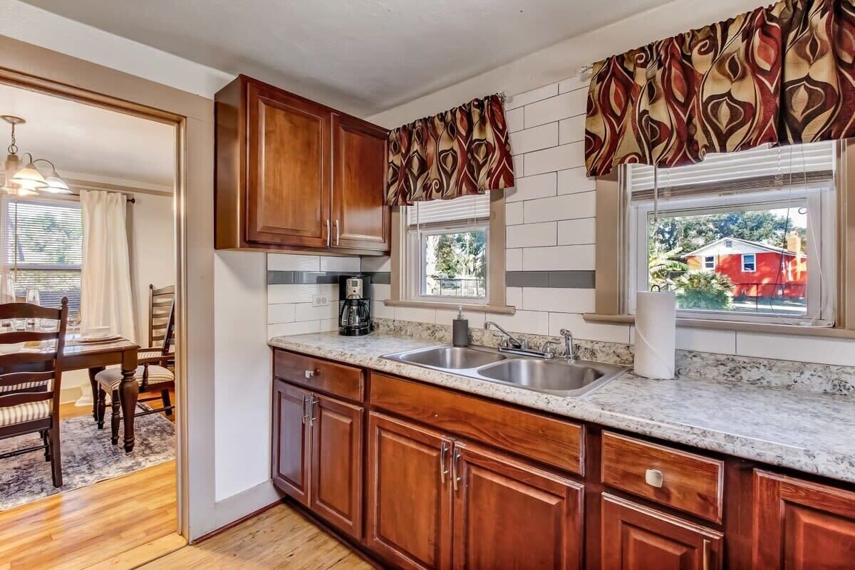 A kitchen with wooden cabinets, a granite countertop, and a window with patterned curtains.