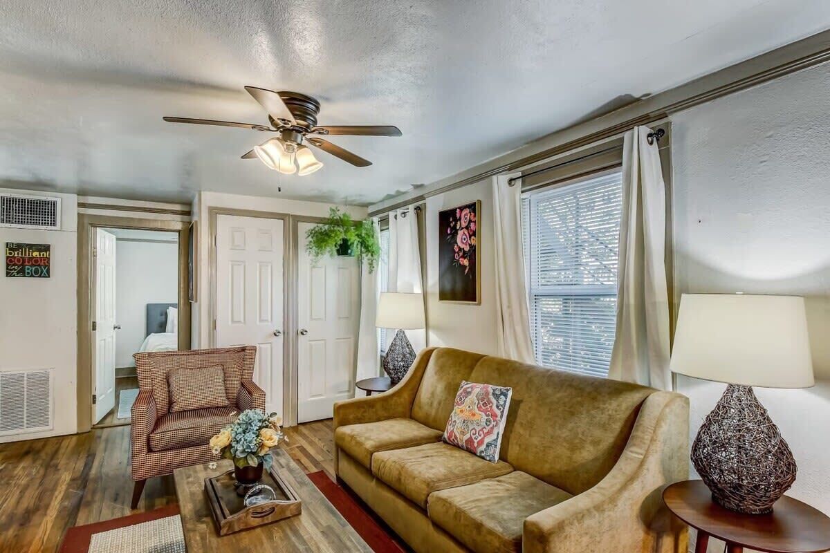 Un salon avec un ventilateur de plafond, un canapé, un fauteuil et une table basse.