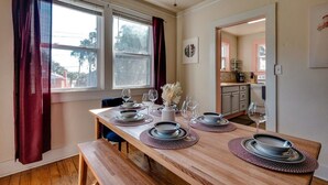 A dining area with a wooden table set for four, a bench, and a view of the kitchen through an open door. - Dock&Volleyball! Near Downtown - Flamingo Flat (Savannah)