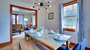 Un coin repas avec une table en bois dressée pour quatre personnes, un banc et une vue sur le salon, accessible par une porte ouverte.