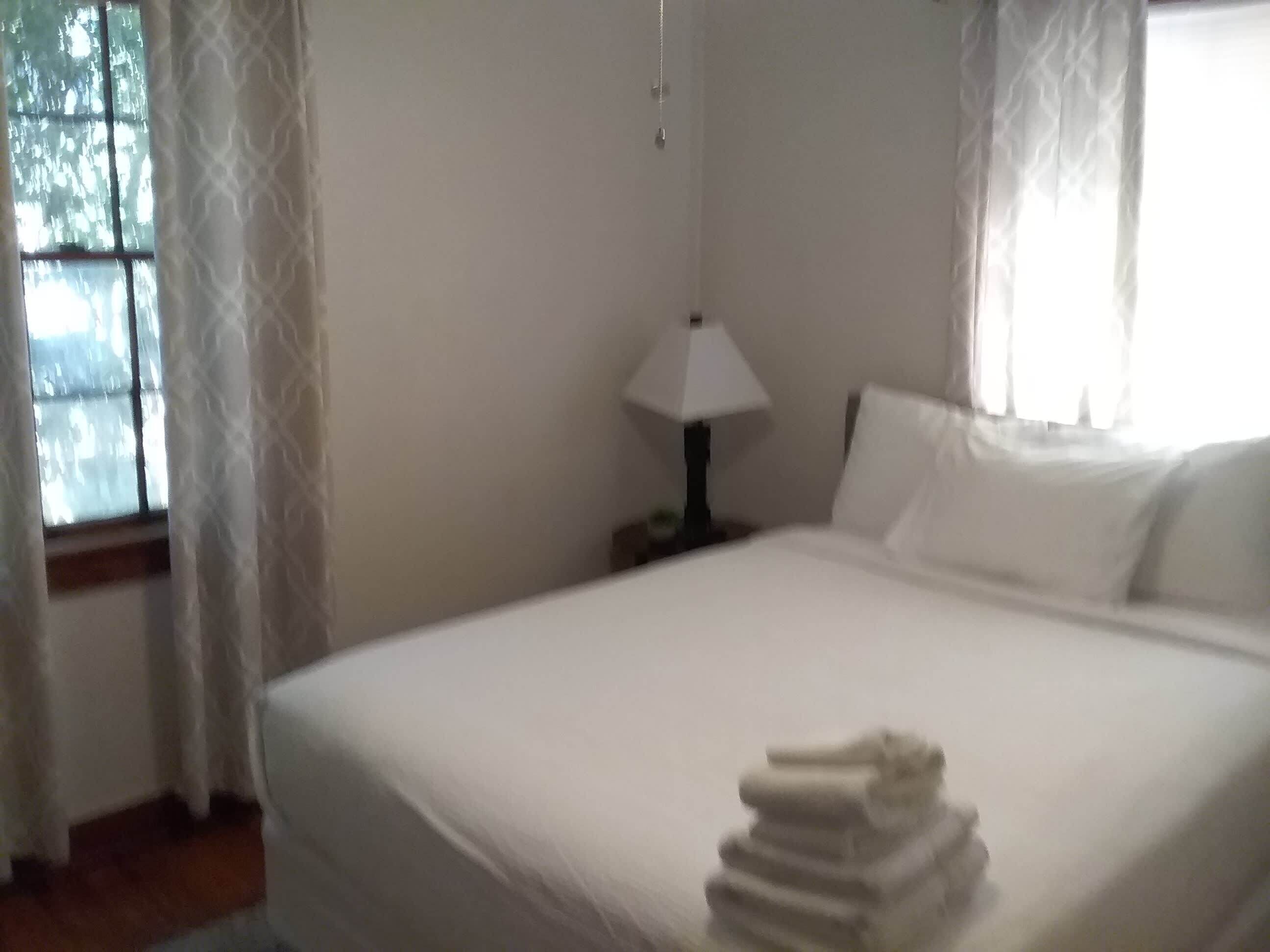 Ett hotellrum med en säng, ett nattduksbord med en lampa och ett fönster med gardiner.