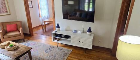 A living room with a television, wooden flooring, a ceiling fan, a sofa, a coffee table, and a lamp.