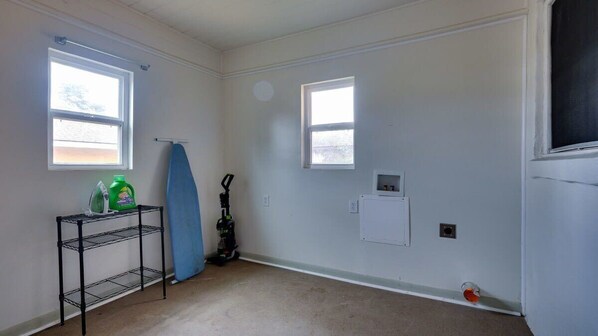 A room with two windows, a metal shelf with cleaning supplies, a vacuum cleaner, and a small electrical outlet on the wall. - Dock & Volleyball! Near Downtown - Golden Getaway (Savannah)