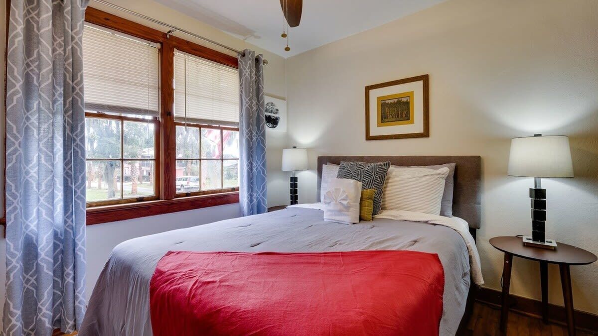 A neatly made bed with a red blanket, two bedside lamps, and a framed picture on the wall.