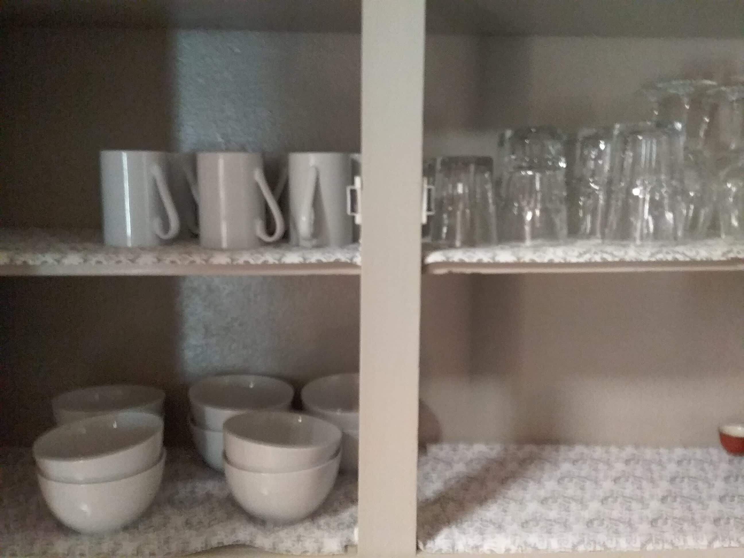 Un estante en la cocina con tazas blancas, cristalería y cuencos.