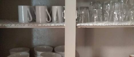 Un estante en la cocina con tazas blancas, cristalería y cuencos.