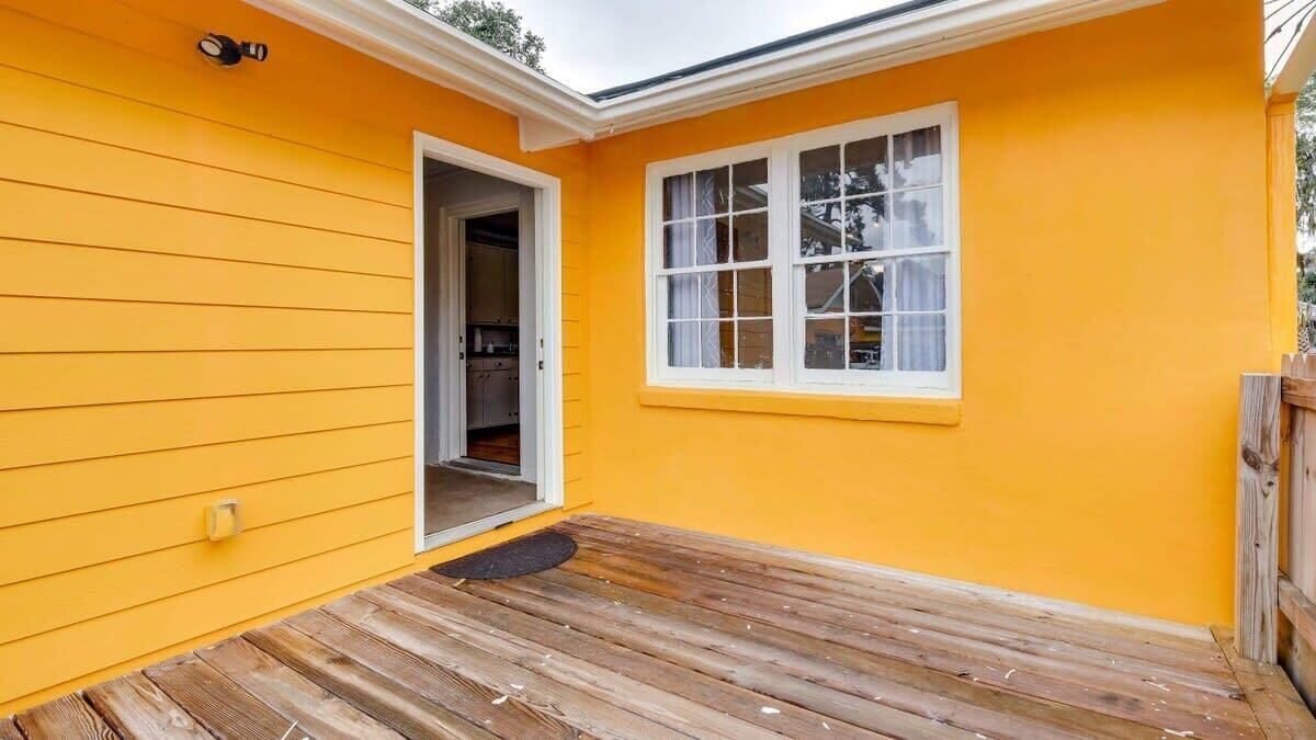 A yellow house with a wooden deck and a white-framed window.