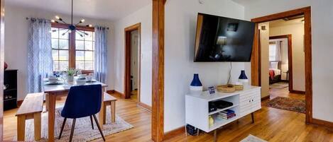 Una sala de estar moderna con comedor, suelo de madera, un televisor de pantalla plana y una consola blanca.