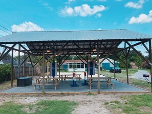 A covered outdoor seating area with picnic tables and benches, surrounded by a wooden fence.
