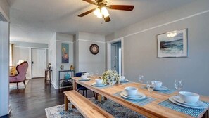 A dining area with a wooden table set for four, a ceiling fan, and a clock on the wall.