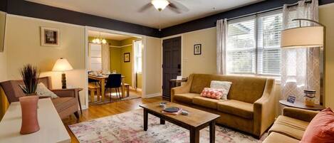 A living room with a sofa, coffee table, and a dining area in the background.