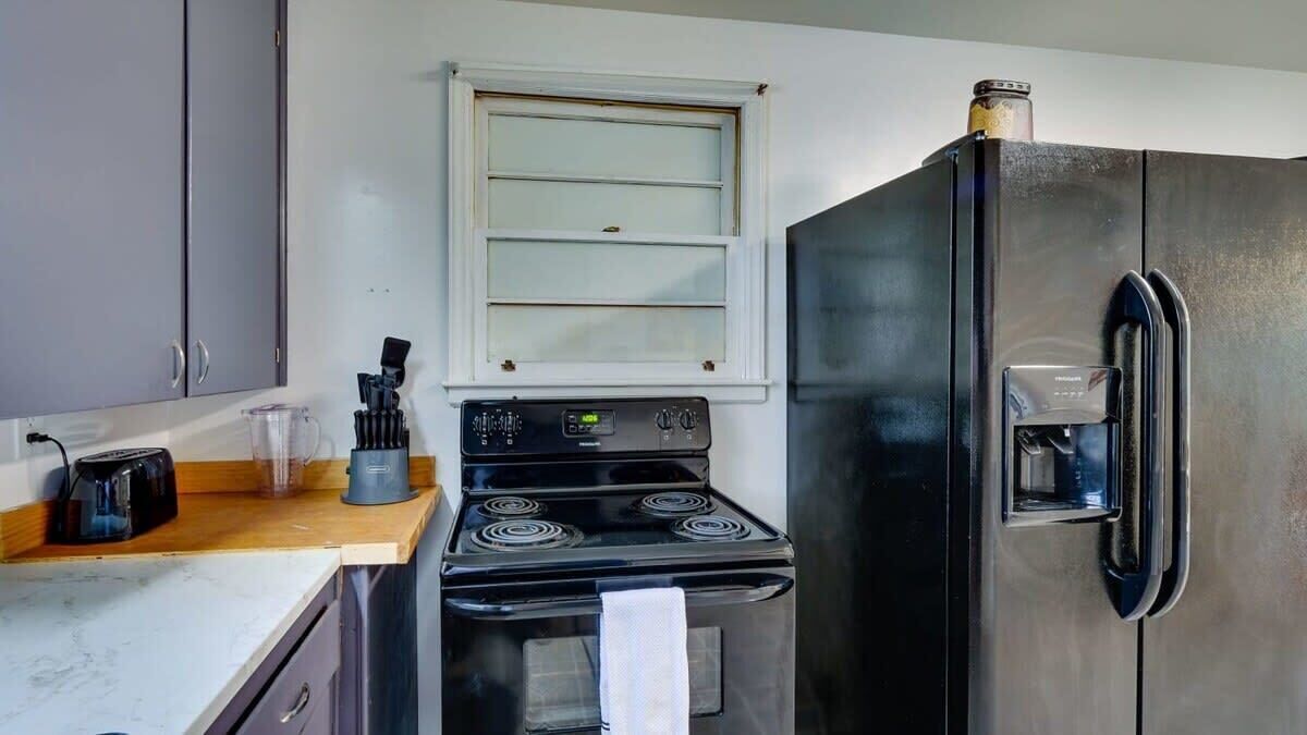 Una cocina compacta con estufa negra, refrigerador y ventana sobre la estufa.