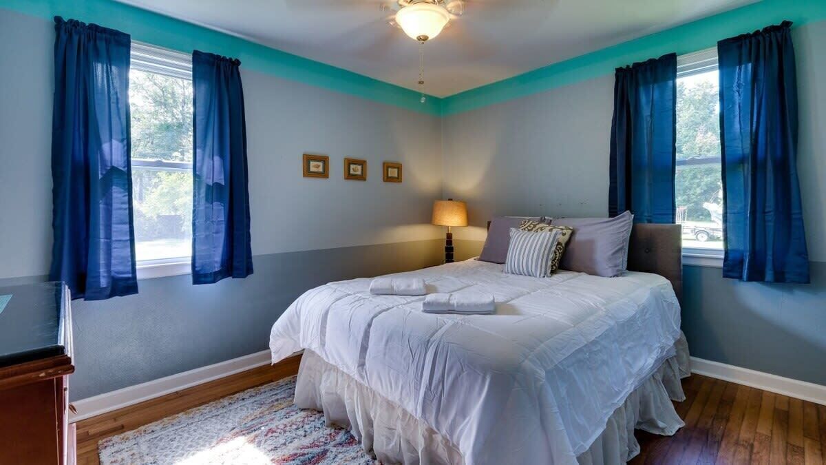 A bedroom with a bed, curtains, a lamp, and a rug.