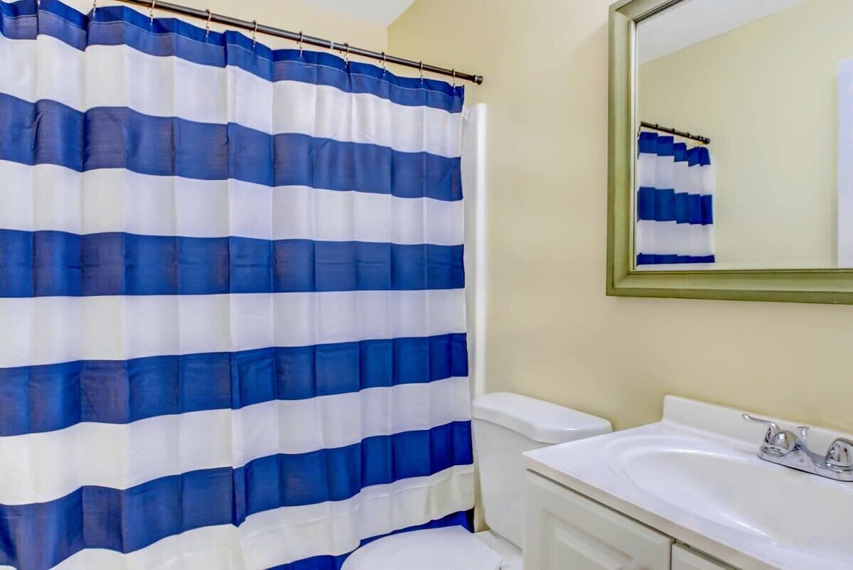 A bathroom with a striped shower curtain, a toilet, and a sink with a mirror above it.