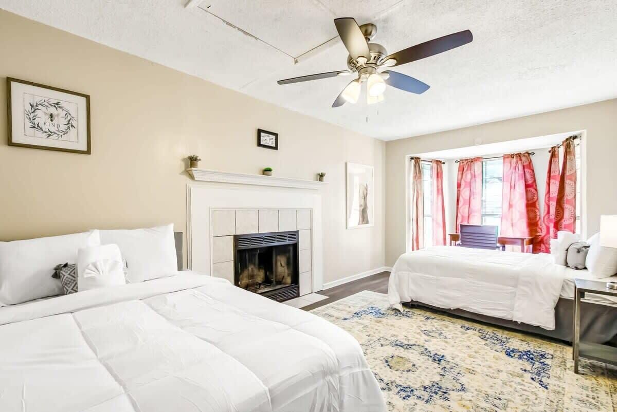 Une chambre d’hôtel avec deux lits, une cheminée, un ventilateur de plafond et une fenêtre avec des rideaux rouges.