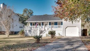 A two-story house with a front porch, a garage, and a small front yard. - Marshside Home with Deck & Pond Access Near Tybee (Savannah)