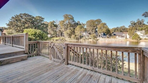 A wooden deck with a railing overlooking a body of water and houses in the background. - Marshside Home with Deck & Pond Access Near Tybee (Savannah)