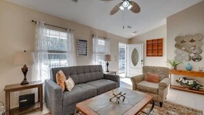 A living room with a grey sofa, a coffee table, a patterned rug, and a ceiling fan. - Marshside Home with Deck & Pond Access Near Tybee (Savannah)
