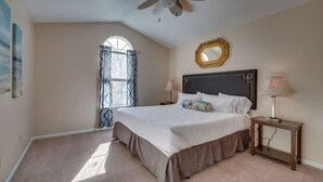 A bedroom with a large bed, a ceiling fan, a window with curtains, and a bedside table with a lamp. - Marshside Home with Deck & Pond Access Near Tybee (Savannah)