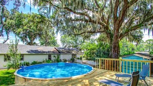 A backyard with a wooden deck, a swimming pool, and a house.