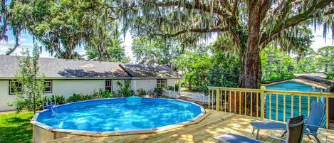 A backyard with a wooden deck, a swimming pool, and a house.