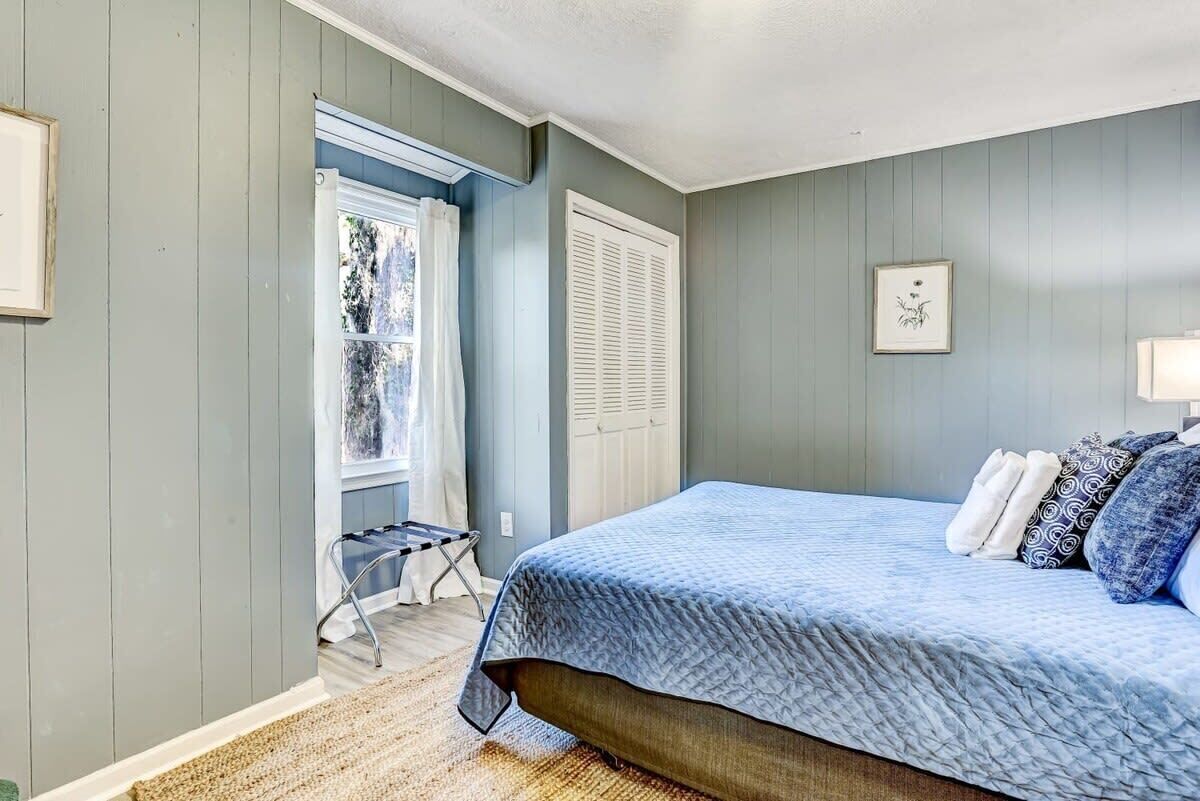 Une chambre à coucher avec un lit, une fenêtre avec des rideaux, une porte et une petite table.