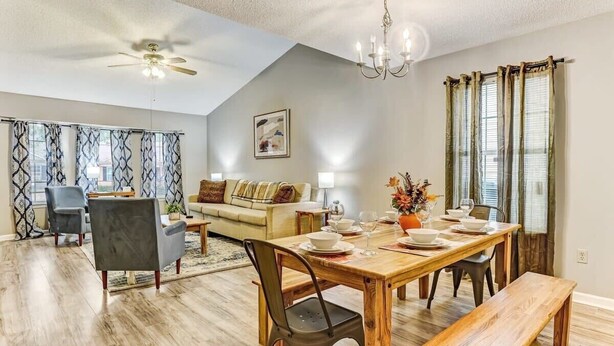 A dining area with a wooden table, chairs, and a bench. There is a ceiling fan, a chandelier, and a dining table set with plates, bowls, and glasses. - Fenced Yard, Patio & BBQ · Historic District Area (Savannah)