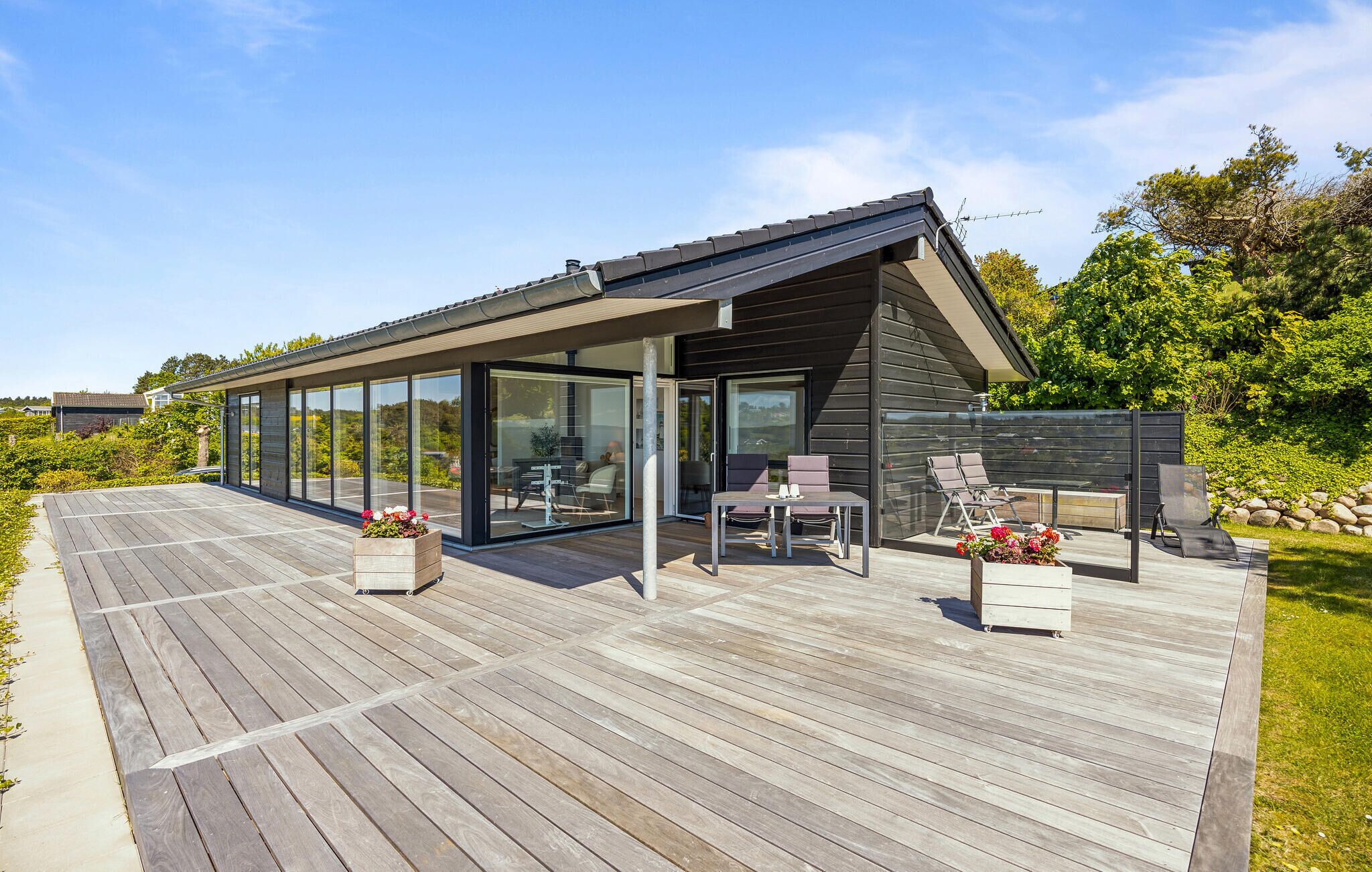 A modern house with a large deck, glass sliding doors, and outdoor furniture.