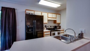 Une cuisine de taille réduite, équipée d’un réfrigérateur, d’une cuisinière, d’un évier et de meubles de rangement en bois.