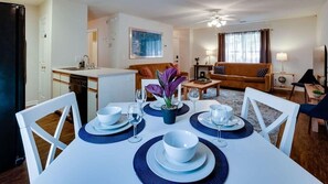 A dining area with a table set for four, a sofa, a coffee table, and a television in the background.