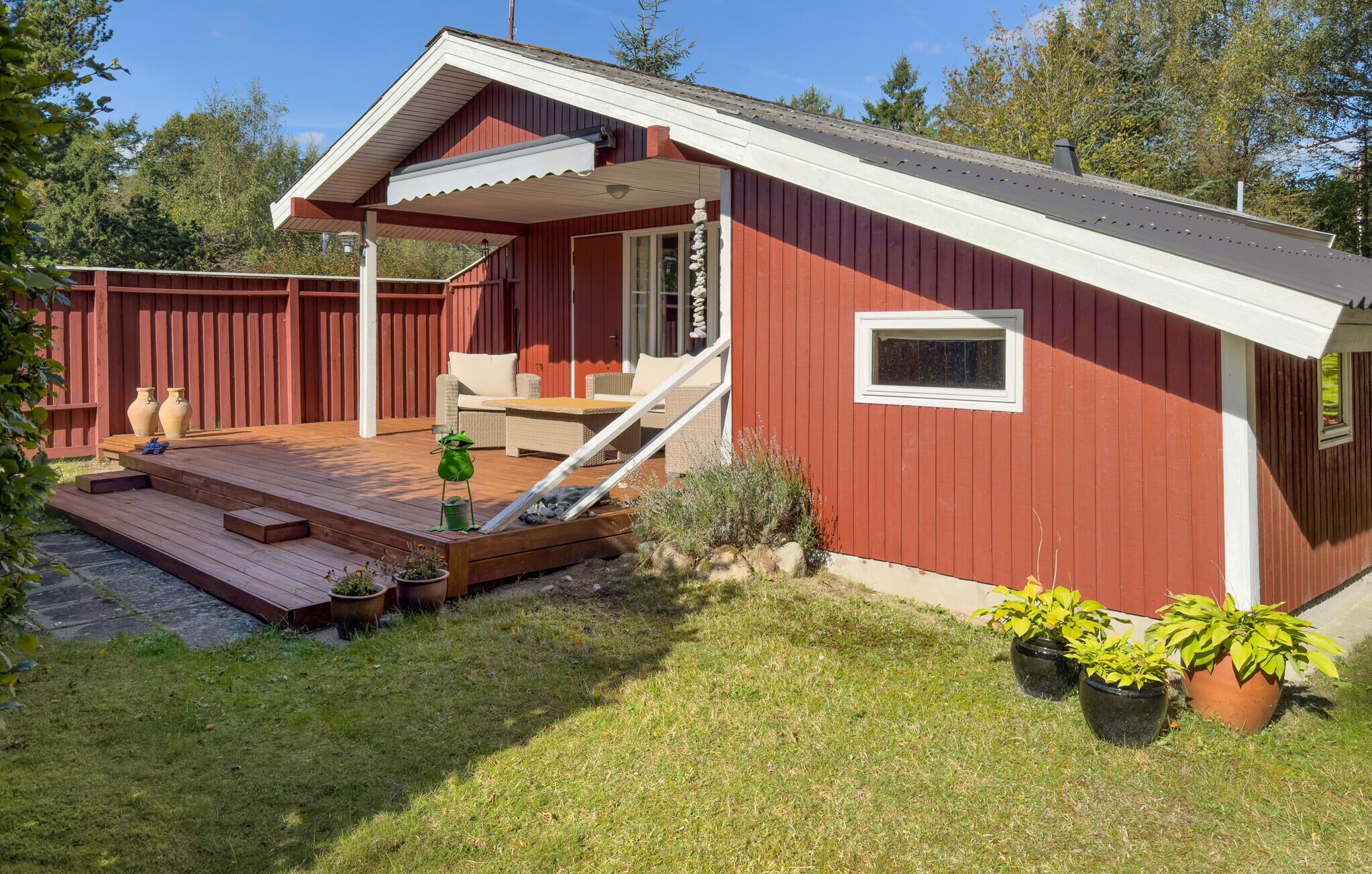 A red wooden house with a porch, a small window, and a staircase leading to the entrance.