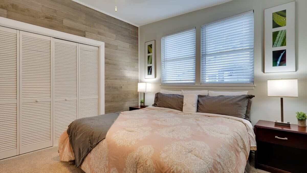 Une chambre à coucher avec un grand lit, deux tables de chevet, une commode, une armoire et une fenêtre avec des stores.