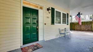 Una casa con puerta verde, número 1305, un porche con dos sillas y una bandera estadounidense.