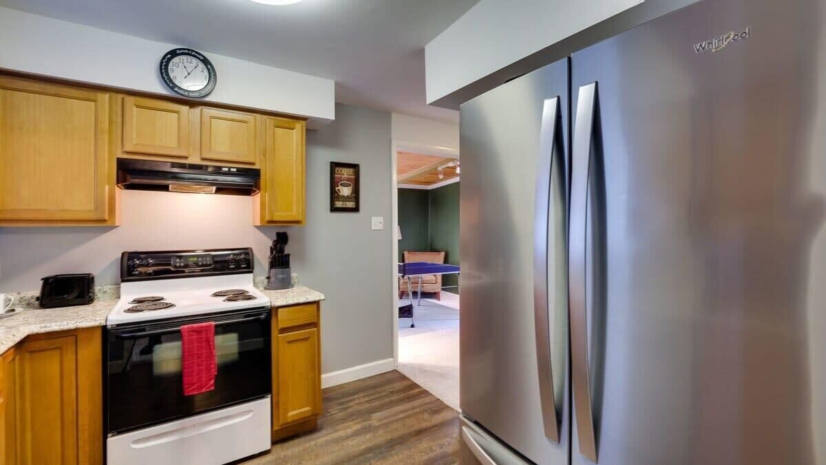 Una cucina con mobili in legno, un frigorifero in acciaio inox, un fornello e una sveglia appesa al muro.