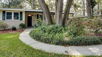 A single-story house with a front porch, a brick foundation, and a well-maintained garden with various plants and flowers.