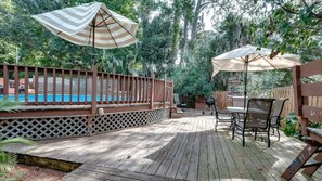 Una terraza de madera con piscina, mobiliario exterior y sombrillas.