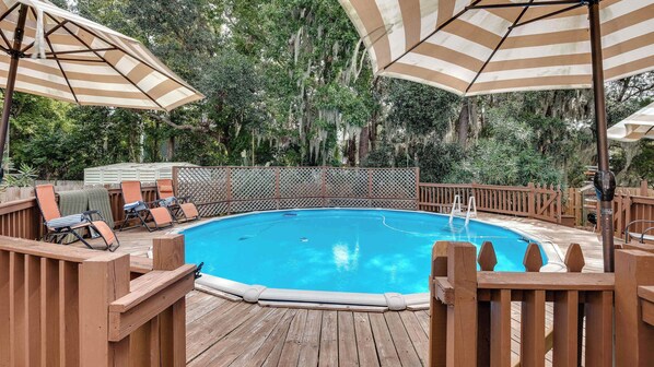 Una terraza de madera con piscina, rodeada por una valla de madera y cubierta por sombrillas a rayas.