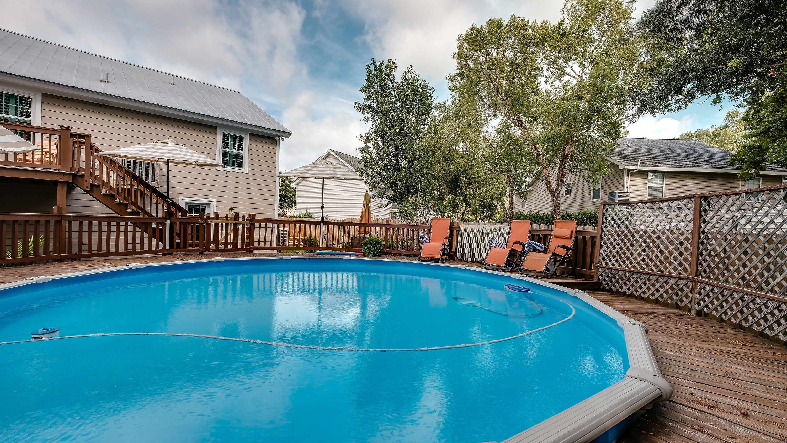 A backyard with a swimming pool, wooden deck, and a fenced area with lounge chairs.