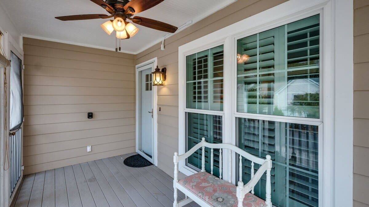 A covered porch with a ceiling fan, a bench, and a large window with shutters.