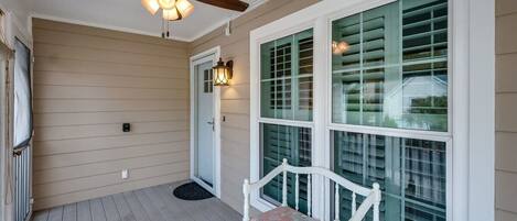 A covered porch with a ceiling fan, a bench, and a large window with shutters.