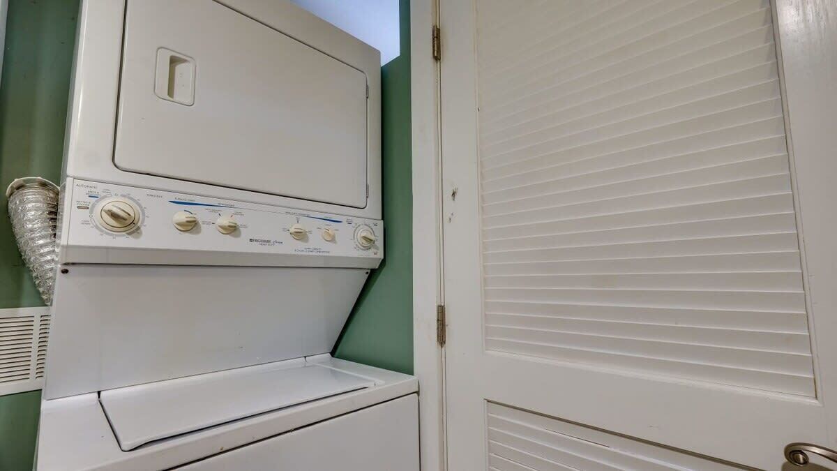 A laundry room with a front-loading washer and dryer, a vent, and a closed door.